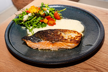 grilled salmon well done over mashed potatoes and served with a salad of lettuce, tomato, mango and cheese.