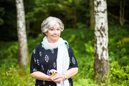 An old grandmother holding a flower outside in the Swedish nature