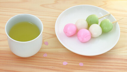 Japanese spring image of three-color mochi sweets and cherry blossom petals on the wood grain background