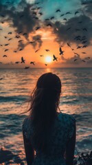 Fototapeta premium Woman watching the sunset on the beach with a flock of birds flying overhead