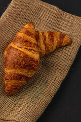 Fresh golden croissants on burlap on black background