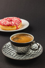 Bright red donut and cup of fresh strong coffee on black background