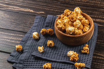 Snack, movie concept, caramelized popcorn in a wooden bowl on a wooden table