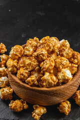 Snack concept, sweet caramelized popcorn in a wooden bowl on a black background