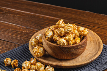 Caramelized popcorn in a wooden bowl with a plate on a wooden background