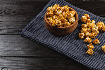 Snack concept, sweet caramelized popcorn in a wooden bowl on a black background