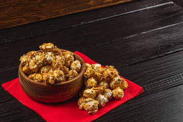 Caramelized popcorn in a wooden bowl with a plate on a wooden background