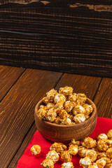 Caramelized popcorn in a wooden bowl with a plate on a wooden background