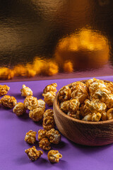 Caramelized popcorn in a bowl on a purple background with golden reflection