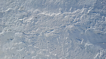A heavily textured white wall surface, with rough plaster or stucco, creates a stark and abstract background with strong light and shadow interplay