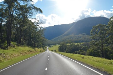Naklejka premium Scenic highway winding through lush green valley and mountains under bright sunlight.