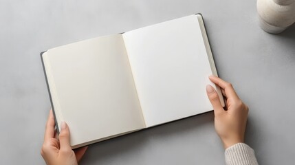 Woman holding open notebook with blank pages at light grey table top view Mockup for design