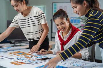 Three female ux designers are collaborating on wireframes for a mobile application, discussing the layout and user interface design while working together in their office