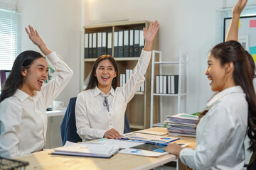 Three enthusiastic businesswomen are raising their hands in celebration during a productive office meeting, expressing their joy and teamwork over achieving a significant milestone