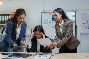 Three asian businesswomen reviewing paperwork, engaged in a tense discussion about a challenging project, feeling the pressure of deadlines and struggling with difficult decisions in the office