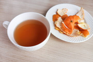 Tea with tangerine peel. A mug of hot tea and a plate with a tangerine peel on the table. Warm drink for colds. 
