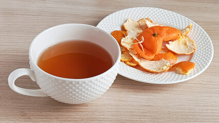 Tea with tangerine peel. A mug of hot tea and a plate with a tangerine peel on the table. Warm drink for colds. 