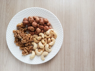 A plate of nuts on a wooden table. Fats in different. Snacking on the Keto diet. Hazelnuts, walnuts, cashews.
