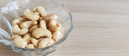 Glass transparent plate with cashews on a wooden table. Fatty amino acids in nuts. Fruits of the evergreen tropical tree Anacardium occidentale.