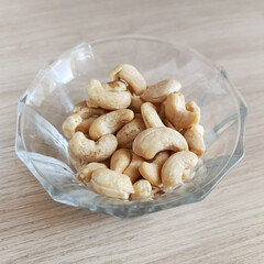 Glass transparent plate with cashews on a wooden table. Fatty amino acids in nuts. Fruits of the evergreen tropical tree Anacardium occidentale.