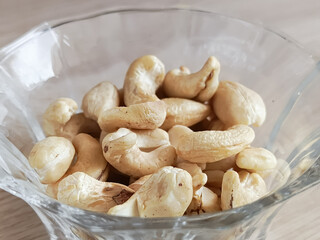 Glass transparent plate with cashews on a wooden table. Fatty amino acids in nuts. Fruits of the evergreen tropical tree Anacardium occidentale.