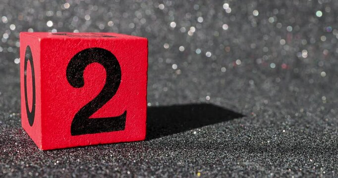 A red block with the number two on it being placed down and lifted back up again on a black glittery background, indicating 2nd birthday or second price concept