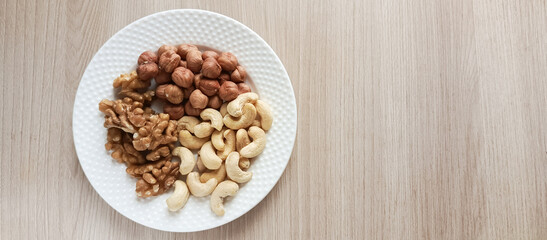 A plate of nuts on a wooden table. Fats in different. Snacking on the Keto diet. Hazelnuts, walnuts, cashews.