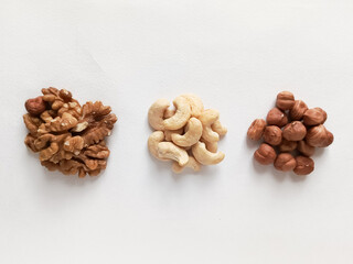 Three types of nuts on a white table. Handfuls of cashews, walnuts and hazelnuts on the table. The benefits of different types of nuts.
