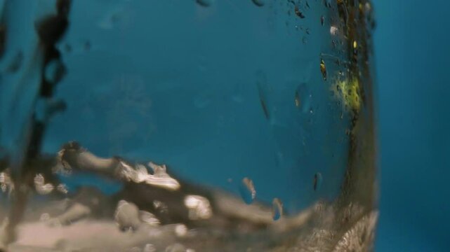 Close-up bubbles in a glass with a blue background. Slow-motion packshot