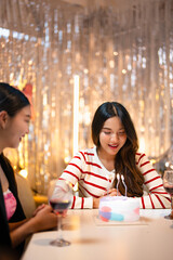Asian people friends having celebration birthday party together at home with food and drink. Woman excited with birthday cake make a wish and blowing birthday candle with happiness.