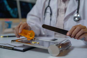 Pharmacist wearing white coat and stethoscope is pouring pills from an orange plastic bottle onto a metal pill counting tray while holding a spatula in the other hand