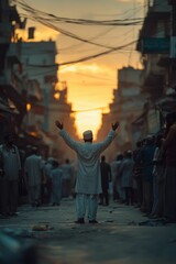 Naklejka premium Man with arms raised, backlit by sunset in crowded street.