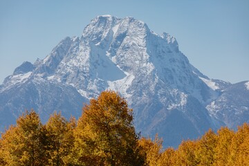 Autumn foliage frames a snow-capped mountain peak. Fall colors contrast with winter's beauty. Grand...