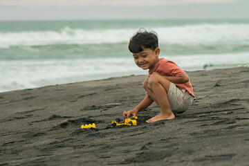 asian boy playing outside with toy cars at the beach. Child, little boy have fun with toy excavator and dumper in the sand