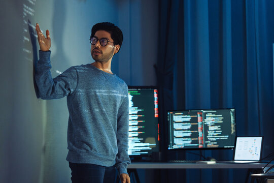 Indian man programmer standing in front of a screen with code projected  presentation the integration of technology and human expertise in software development
