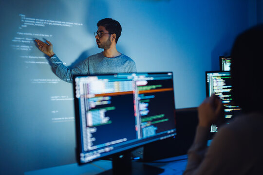 Indian man programmer standing in front of a screen with code projected  presentation the integration of technology and human expertise in software development