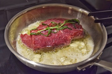 A piece of beef is fried in a frying pan in oil with garlic. Cooking at home.
