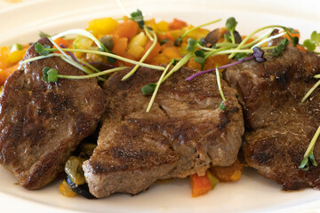 Meat, beef medallions with vegetables on a plate with microgreens.