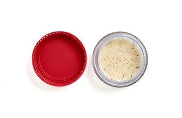 Opened lip scrub in small glass container with pink cap next to it isolated on horizontal white...