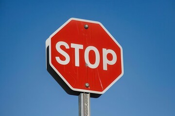 Obraz premium A red octagonal stop sign against a clear blue sky, indicating a traffic regulation.