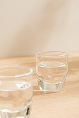 Glass of water isolated on wooden background. Warm lighting background. Wooden surface. Light and Shadow wallpaper. Space for text. Backdrop. Studio photography. Still life. 