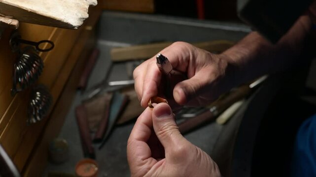 Skilled goldsmith carefully shaping delicate gold ring using specialized precision tools inside traditional metalworking workshop. Craftsmanship