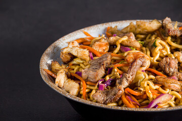 Yakisoba mixed with beef and shrimp, stuffed with assorted vegetables such as beetroot and carrots in a rustic dish on a black table with texture close-up photo with texture