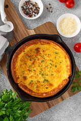 Savory cheese Dutch baby pancake. Dutch Baby pancake with mix tomatoes, parsley and arugula in cast iron pan on a concrete background. Delicious healthy breakfast.