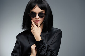 Beautiful woman with black hair wearing sunglasses and a black blazer, posing confidently against a...