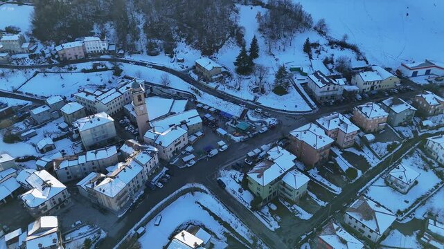 Aerial view capturing Morfasso, a charming village nestled in the Apennine Mountains near Piacenza, blanketed in snow under a bright, sunny winter sky, drone shot