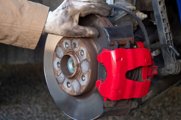 Person is working on a car's brake system, specifically the brake caliper. The caliper is red and has a black handle. The person is wearing gloves while working on the car