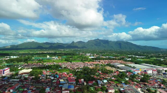 Aerial view across Lipa City in Batangas with rooftops industrial buildings green plains and mountain ridges under a cloud filled sky