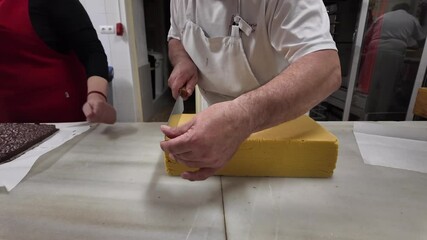Closeup view of the hands of a white pastry chef cutting a block of traditional turron sweet for Christmas over a white marble table in his workhop. 4K