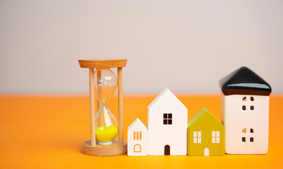 Miniature figures of houses and sand hourglass. Mortgage and loan concept. Temporary rental housing...